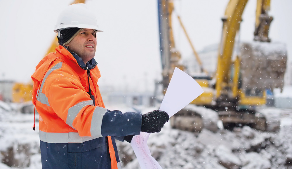 Site worker wearing PPE and holding guide with wintery background