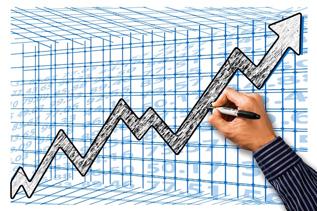 Hand drawing a graph on blue background, with an upwards data trend 