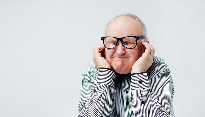 Senior man wearing glasses and holding his ears symbolising loud noise pollutions