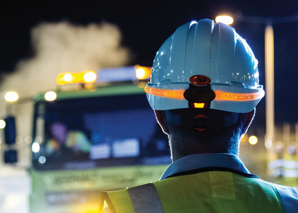 Construction worker wearing hi-vis and white hard hat with illumination band for more visibility