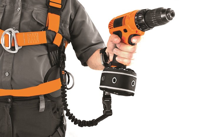 Male wearning orange harness holding a power drill that is tethered with a tool lanyard for drop prevention