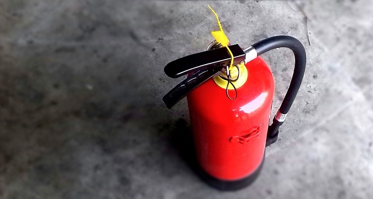 Red fire extinguisher leaning against a grey wall