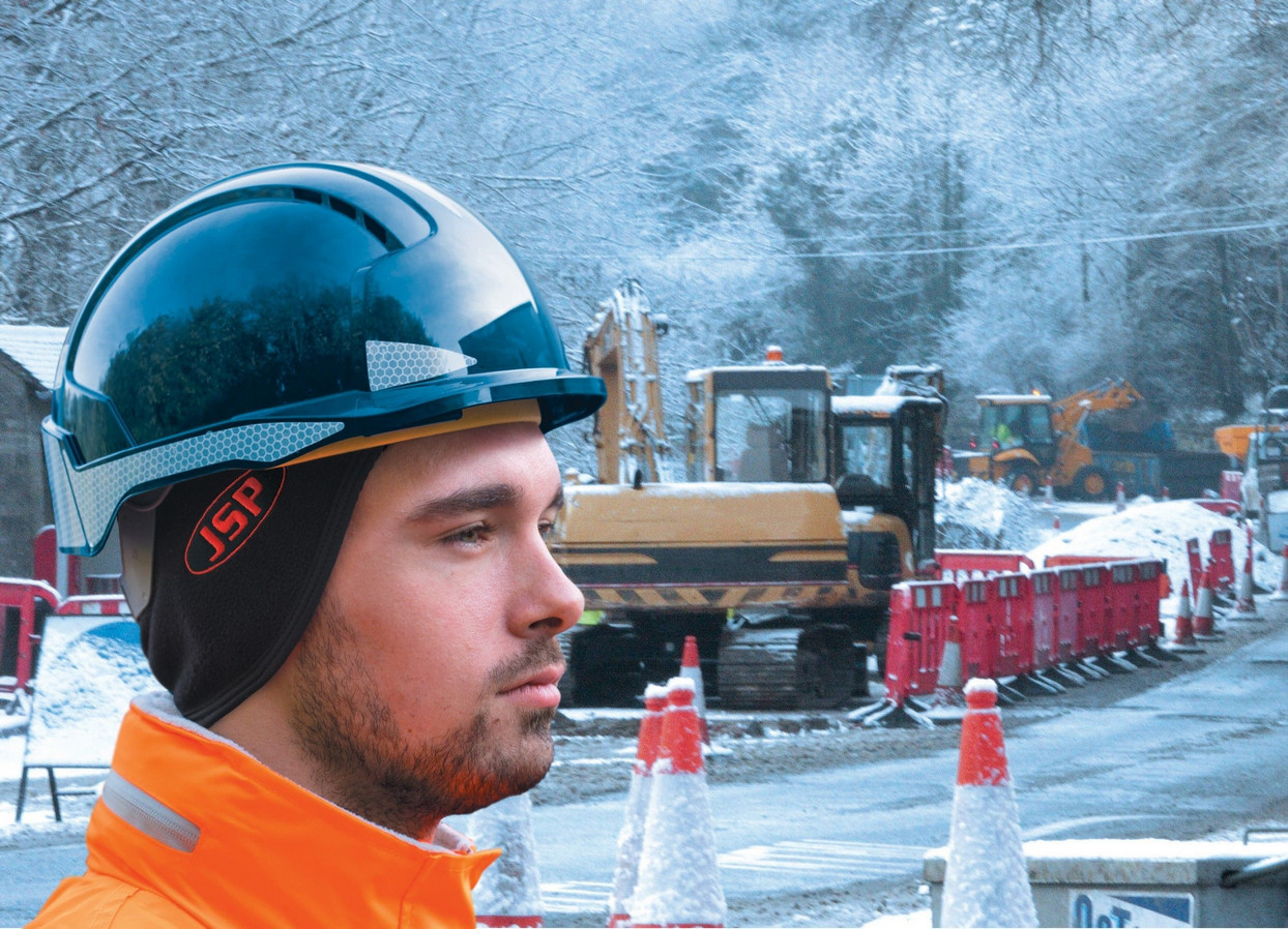 Site operative wearing JSP thermal beanie under his black safety helmet with winter background